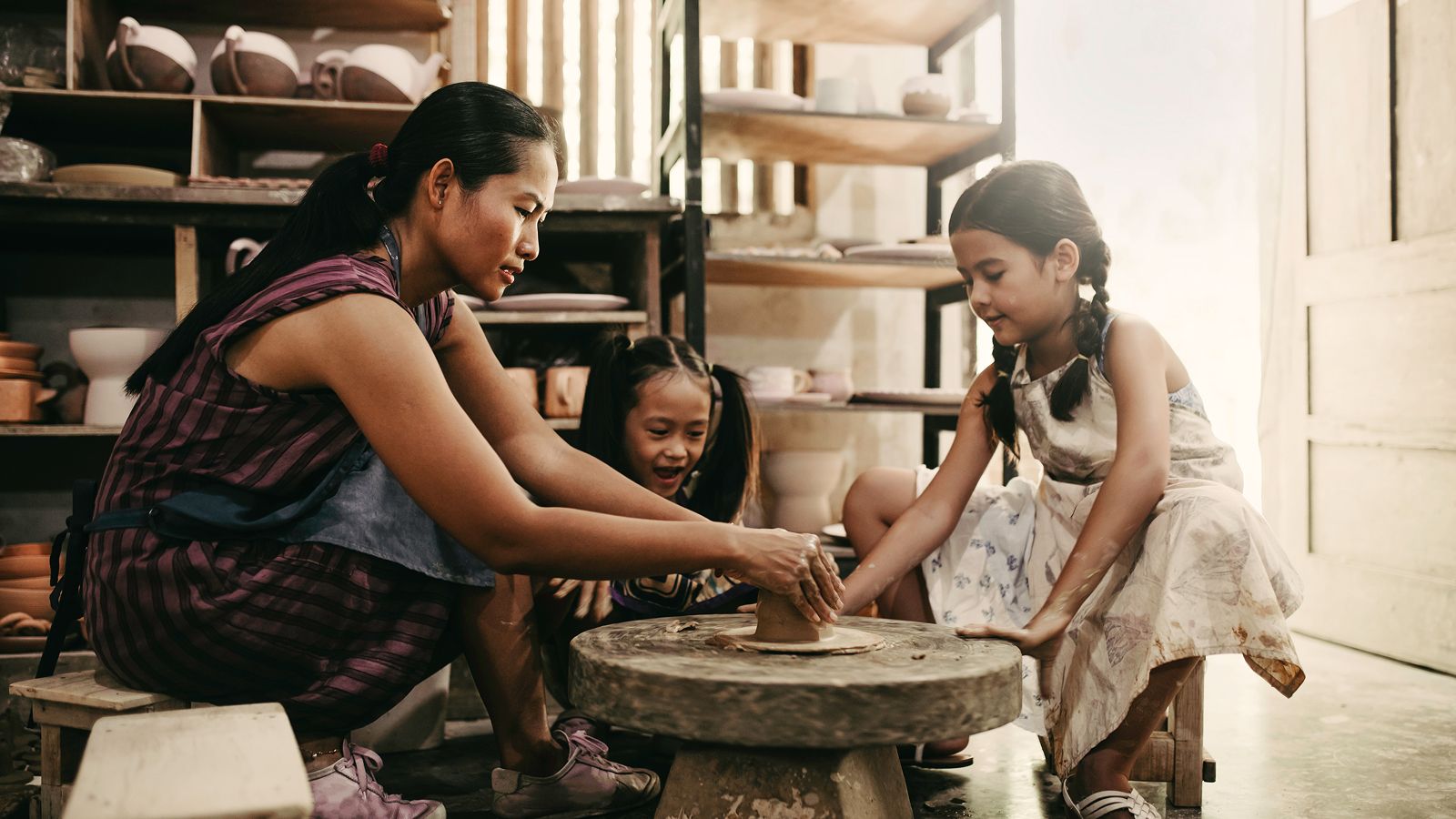 Woman and two youn ghildren work on pottery wheel