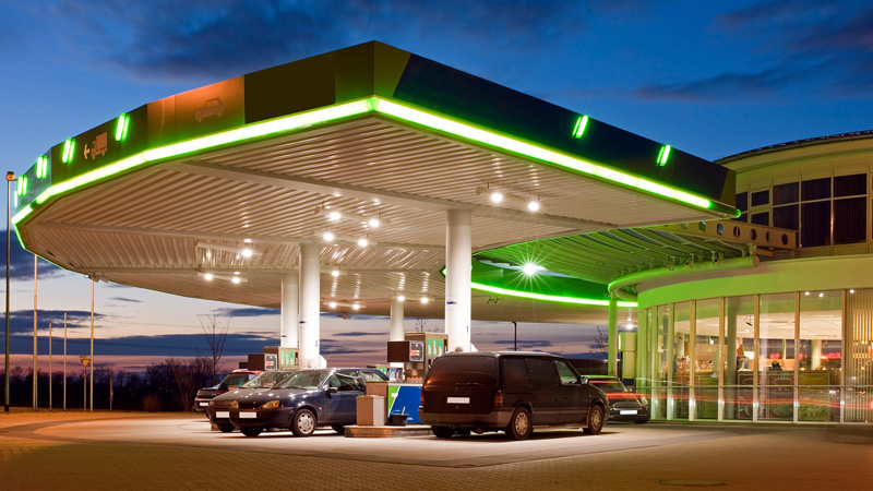 Gas station with all lights on and vehicles at gas pumps.
