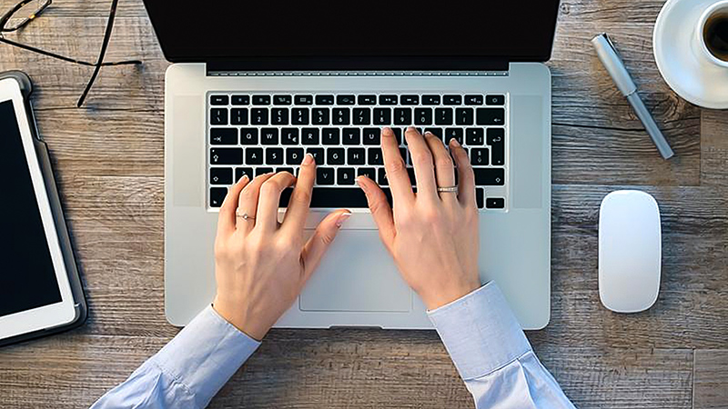 Mãos de um homem sobre o teclado de um laptop, prontas para digitar