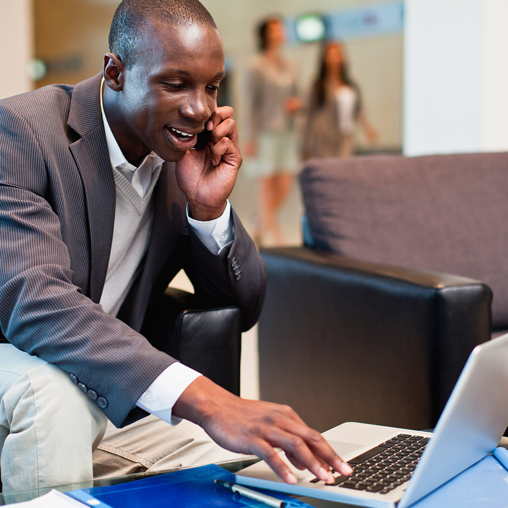 Seated man using mobile phone and laptop.