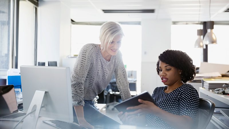Two women inside an office looking at a tablet.