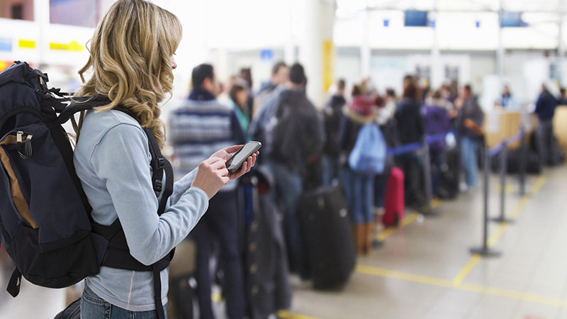 Travelers with luggage standing in long line.