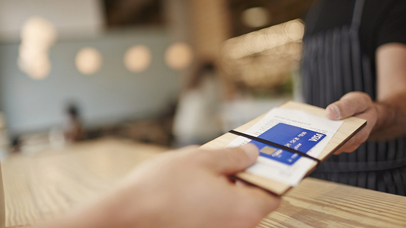 Customer handing Visa card and tab to restaurant worker.